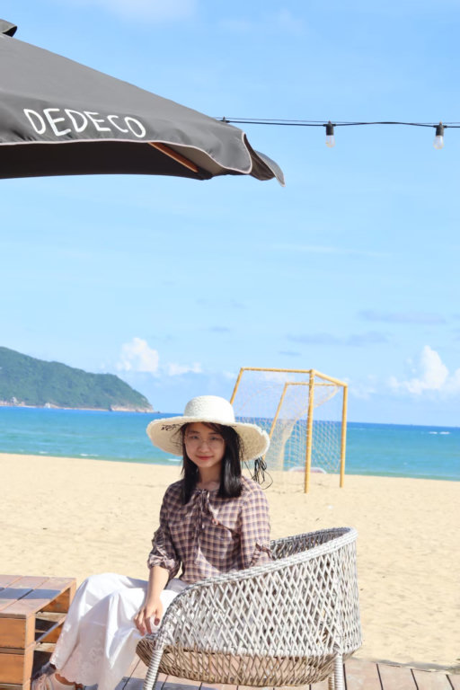 Yuan Tian seated on a beach in a sun hat